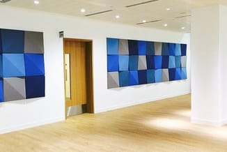 Moderne kantoorruimte met houten deur, laminaat vloer en twee blauwe akoestische wandpanelen in geometrische patroon.