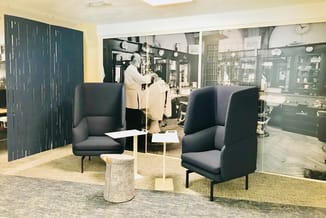 Twee zwarte fauteuils met hoge rugleuning en metalen poten tegenover elkaar in een moderne kantoorruimte met donkergroene sch