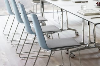 Moderne vergaderruimte met lichtblauwe bezoekersstoelen op wielen, grijze zitplaten en chromen frames, naast witte vergaderta