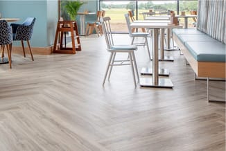 Modern kantoor met lichte houten vloer, witte tafel, grijze stoelen, houten accenten en blauwe muurpaneel, uitzicht op groen