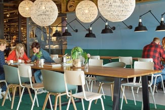 Kantoorruimte met houten vergadertafel, witte en mintgroene stoelen, hangende weefsel- en zwarte industriële lampen, groen-bl