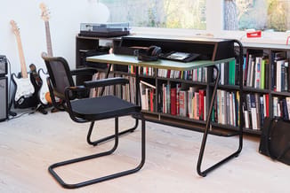 Donker bureau met boekenkast, zwarte bureaustoel en gitaren in thuiskantoor met houten vloer.