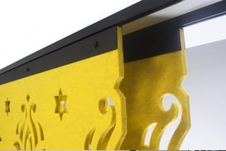 Gele akoestische panelen met decoratieve uit-/inschuifbare lamellen en sterpatronen, gemonteerd onder zwarte railsysteem.