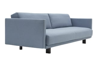 Grijsblauwe stofbank met rechte armleuningen, lage zwarte poten en minimalistisch design, frontaanzicht.