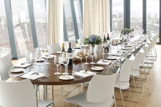 Moderne vergadertafel in donker hout met witte stoelen, volledig gedekt voor een diner met glazen, bestek en servies. Uitzich