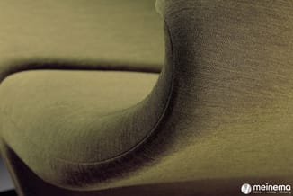 Detailopname van een grijsgroen gestoffeerde zitmeubel met zichtbare weave-structuur en donkere welting.