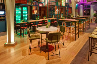 Modern ingerichte lounge met ronde tafel, groene stoelen, houten tafels, groene glazen kasten en paarse wandverlichting op ho
