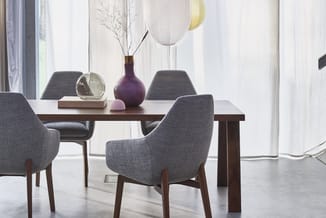 Houten eettafel met grijze stoelen in modern interieur, versierd met vazen en decoratieve objecten, grote ramen op achtergron