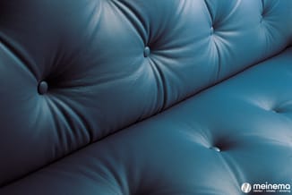 Blauwe gestoffeerde bank met kapitonnage en decoratieve knopen in detail weergegeven.
