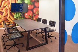 Moderne vergaderruimte met grijze tafel, zwarte bureaustoelen en wanddecoratie met groenten en blauwe cirkels. Aan muur gemon