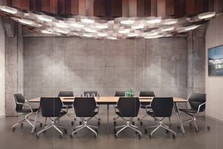 Moderne vergaderruimte met lange houten tafel, zwarte bureaukstoelen op wielen, betonnen wanden en geometrisch plafondlicht.
