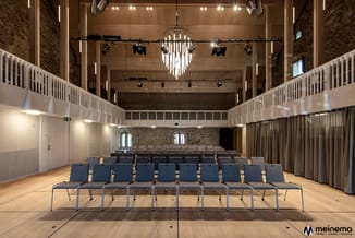 Moderne vergaderruimte met blauwe stapelstoelen in rijen, houten vloer, witte balustrades op galerijen, hangende designverlic