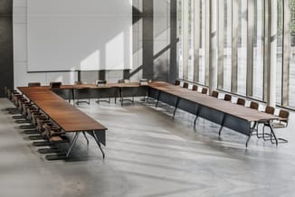 Moderne vergadertafel in U-vorm met houten blad en zwarte onderkant, omgeven door bruine stoelen met zwarte poten in grote li