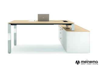 L-vormig bureau met licht houten blad, witte onderkast met lades en grijze metalen poten. Laptop en accessoires op tafelblad.