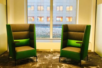 Twee groene fauteuils met bruin binnenkant in kantoorruimte met grote ramen uitzicht op strand en gebouwen.