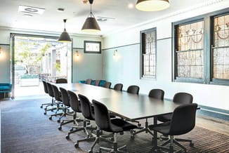Moderne vergaderruimte met lange witte tafel, zwarte bureaustoel op wielen en hangende metalen lampen boven.