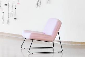 Roze gestoffeerde loungefauteuil met zwart metalen frame op minimalistisch witte galerieruimte met hangdecoratie.