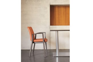 Oranje bureaustoel met donker houten frame in moderne kantoorruimte met betonnen wanden en stalen tafelonderstel.