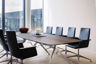 Moderne vergaderruimte met houten tafel, zwarte en grijze vergaderstoelen, roestvrijstalen poten, grote ramen en rode bloemen