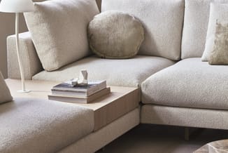 Beige modulaire hoekbank met verschillende kussens, houten tafel met boeken en decoratie, witte staande lamp, minimalistische