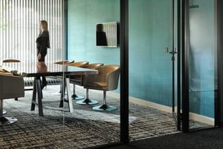 Moderne kantoorruimte met groene glazen wand, houtentafel, grijze stoelen en daglicht via verticale lamellen.