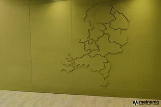 Gele wandpanelen met ingefreesd kaartontwerp van Nederland, houten vloer zichtbaar, moderne kantoorinrichting.
