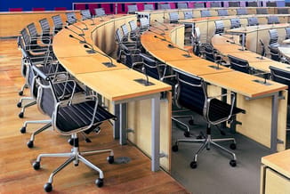 Kantoorruimte met houten bureaus, zwarte ergonomische bureaustoelen en microfoons, houten vloer, blauwe en rode wanden op ach