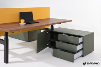 Bruin bureau met geel scherm, zwarte poten en grijsgroen ladeblok met drie laden, laptop en gele koffiemok.