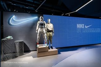 Nike Citadium Parijs | Uitstalruimte met twee mannequins op houten podium, grijze cilindervormige poefs, blauwe wandbekleding