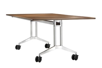 Mobiele vergadertafel met trapeziumvormig houten blad in houtkleur, wit metalen onderstel en zwarte wielen.