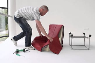 Man assembleert rode fauteuil in moderne kantoorruimte. Gereedschap op vloer, bijzettafel en ergonomische stoel op achtergron