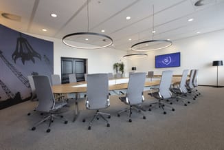 Moderne vergaderruimte met lange houten tafel, grijze bureaustoelen, hangende ringvormige verlichting en een display met "Nor