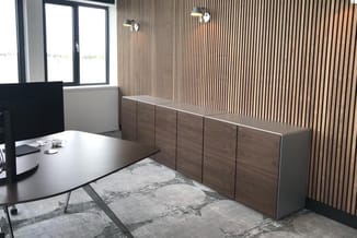 Kantoorruimte met houten kastenwand, bureau, raam, gestreepte wandbekleding, verlichting en grijze vloertegel.