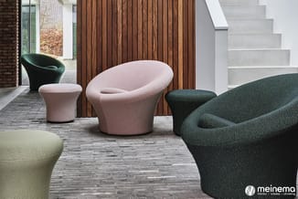 Moderne loungefauteuils in roze, groen en geel met ronde vormen op houten vloer in kantooromgeving met trap.
