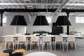 Modern kantoor met lange witte tafel, witte stoelen met zwarte zitting, drie zwarte hanglampenkappen boven tafel en akoestisc