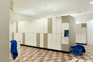 Kleedkamer met witte en beige kasten, zwarte sokkel, blauwe handdoeken en wasmandje op diamantvormig tegelvloer.
