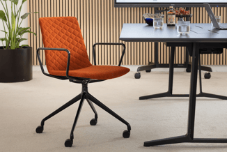 Wiesner-Hager Nooi conferentiestoel met rood-oranje bekleding, ruitstiksel, armleuningen en zwart kruisvoetonderstel op wielen naast een vergadertafel.