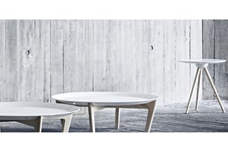 Drie witte ronde tafels met lichte houten poten in minimalistisch interieur tegen grijze houten wand.