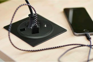 Zwart wandcontactdoos met USB-poort en ingebouwde kabelorganizer, aangesloten op smartphone via gevlochten kabel op lichte ho