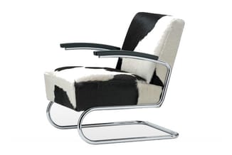 Moderne fauteuil met zwart-wit koeienprint bekleding, chromen frame en armleuningen, op sledevoet.