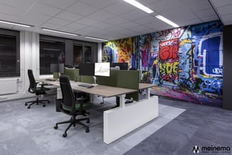 Modern kantoor met grijze werkplekken, groene bureauschermen, zwarte ergonomische stoelen, witte werkbladen en graffitikunst
