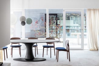 Ronde zwarte vergadertafel met witte blad en houten stoelen met blauwe zitting in moderne kantoorruimte met grote ramen.