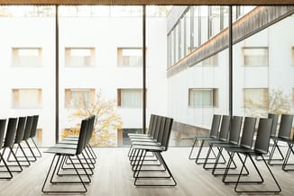 Moderne vergaderruimte met zwarte kantelstoelen op metalen frames, grote ramen, witte wanden en houten accenten.