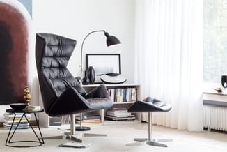 Zwarte leren loungestoel met hoge rug en voetsteun in minimalistisch kantoor met arclamp, bureau met schappen en grote ramen.