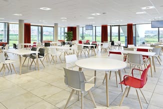 Moderne kantoorruimte met witte ronde en rechthoekige tafels, houten poten, rode en grijze stoelen, grote ramen met rode gord