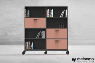 Zwart kastenstelsel op wielen met gemengde opbergvakken en roze gesloten deuren, gevuld met boeken en decoratieve objecten.