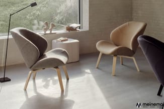 Moderne lounge met grijze en beige stoelen met houten poten, witte zitpoef, raam, staande lamp en boeken op tafel.