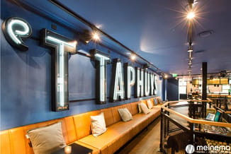 Lounge area met oranje lederen bank, blauwe wand en witte neonletters "TAPAS", verlicht kantoorinterieur.