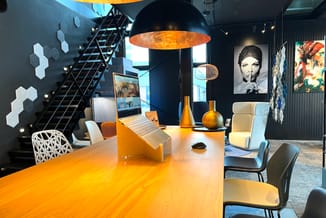 Modern kantoor met houten vergadertafel, witte en zwarte stoelen, zwarte hanglamp met gouden binnenkant, laptopstandaard, lou