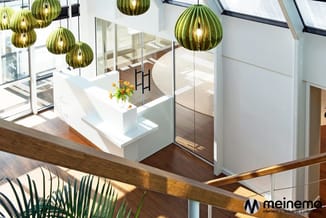Moderne kantoorruimte met groene hangllampen, wit receptiebalie met gele bloemen, glazen wanden en houten railing op mezzanin